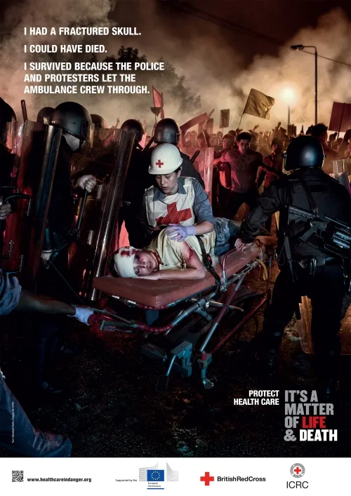 ICRC 'Health Care in Danger' poster — a medic evacuating a head-injured casualty through a riot, 'It's a Matter of Life & Death'
