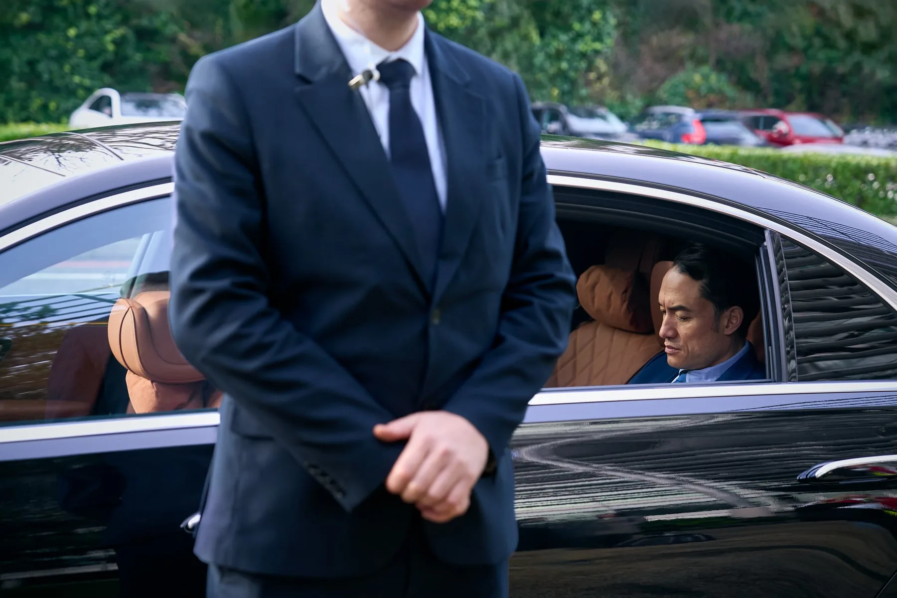 A close-protection officer beside a chauffeured car, executive seated inside — International SOS