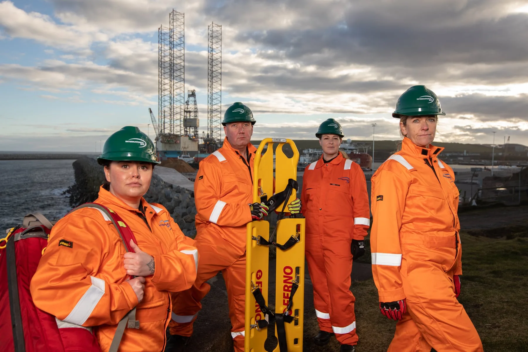 Four International SOS responders in hard hats with a rescue stretcher at an offshore-rig harbour in Aberdeen