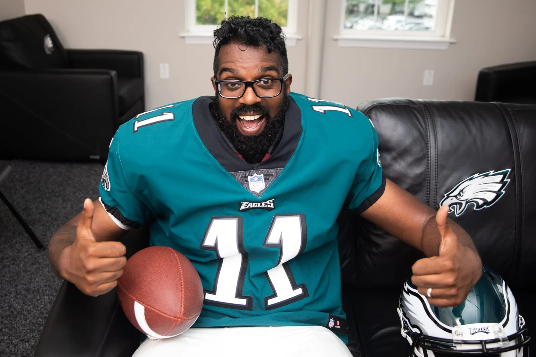 Comedian Romesh Ranganathan giving a thumbs-up with a football and Eagles helmet — Sky's 'Rob & Romesh Vs'