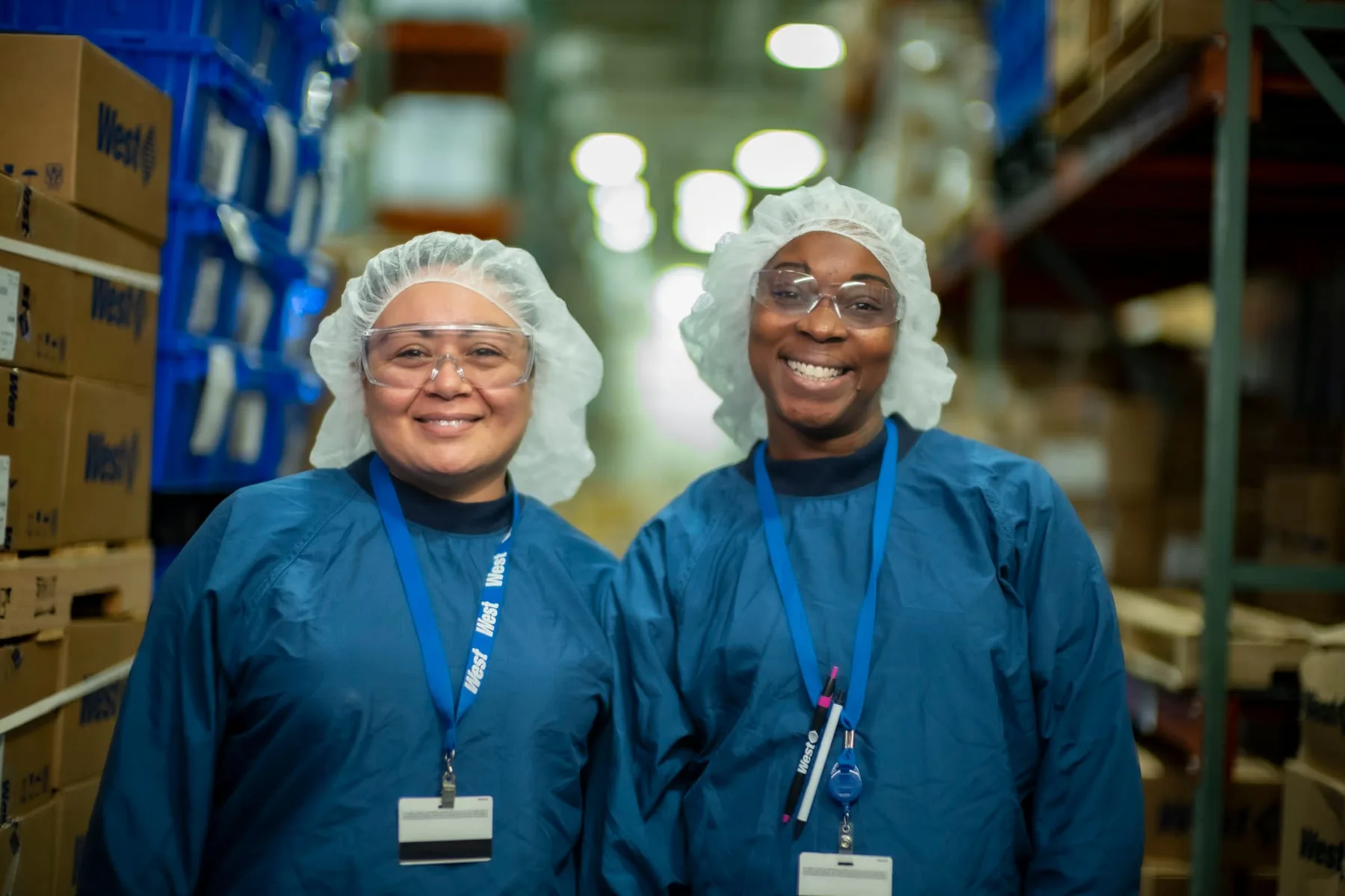 Two West Pharmaceuticals colleagues in gowns and safety goggles in a packing warehouse in North Carolina
