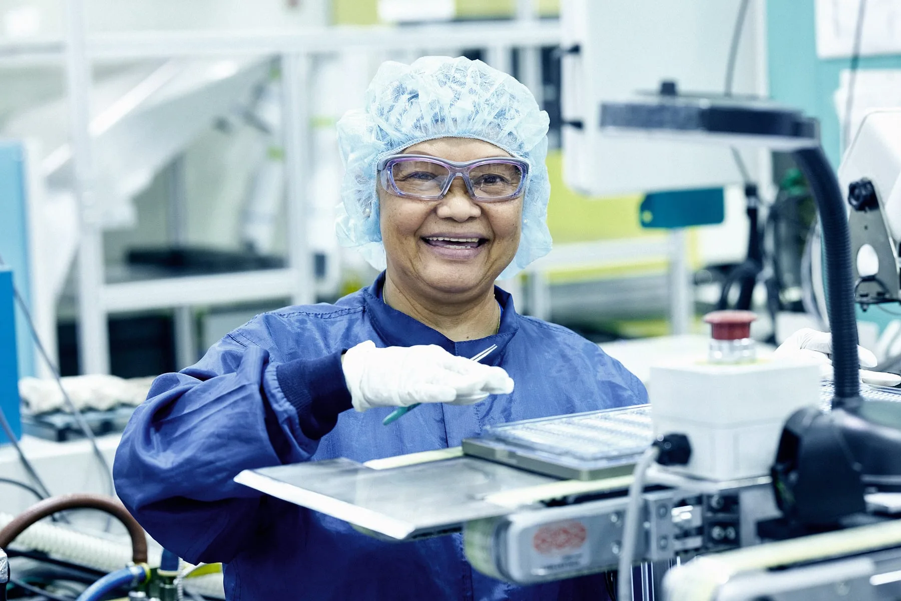 A West Pharmaceuticals cleanroom operator in gown, hairnet, safety goggles and gloves at her production station, Arizona